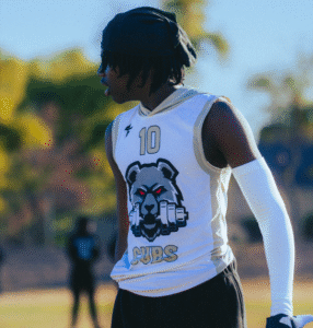 Athlete in a white Cubs jersey seen from behind on the sideline