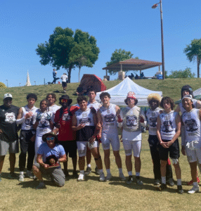 Team and families gathered under a canopy at an outdoor event
