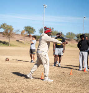 Coach throwing a football to an athlete during field practice